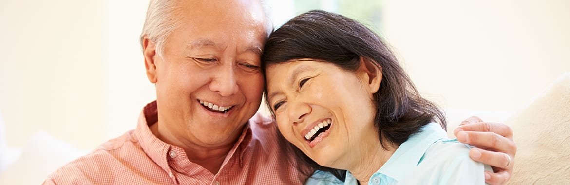 Older Asian couple smiling and embracing.