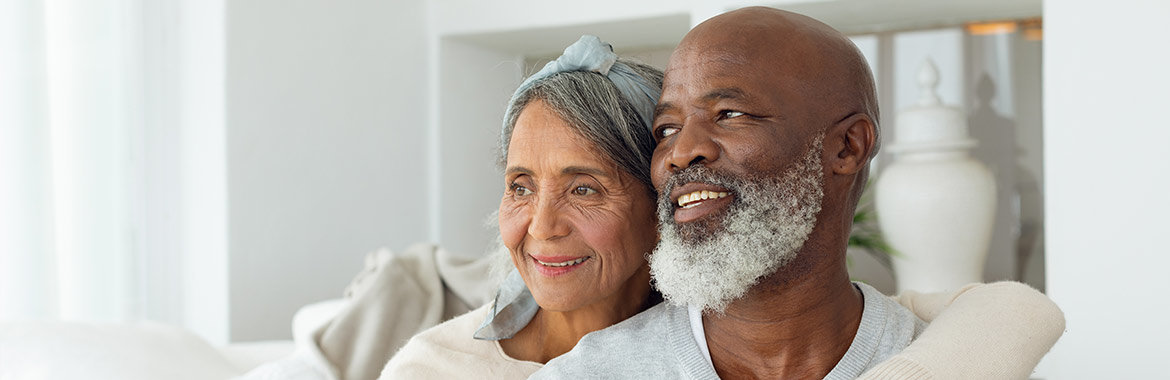 Senior African American couple sitting on couch smiling.