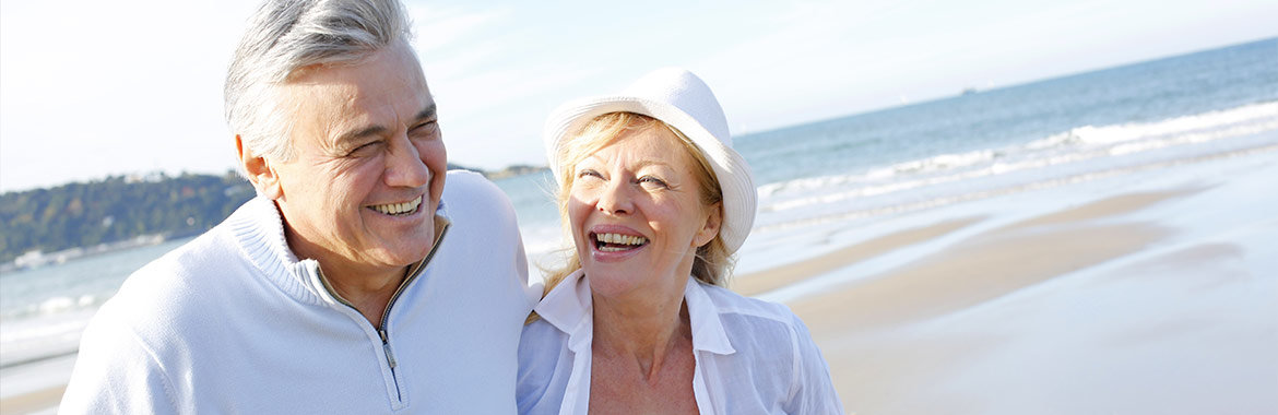Older couple laughing and walking on beach.