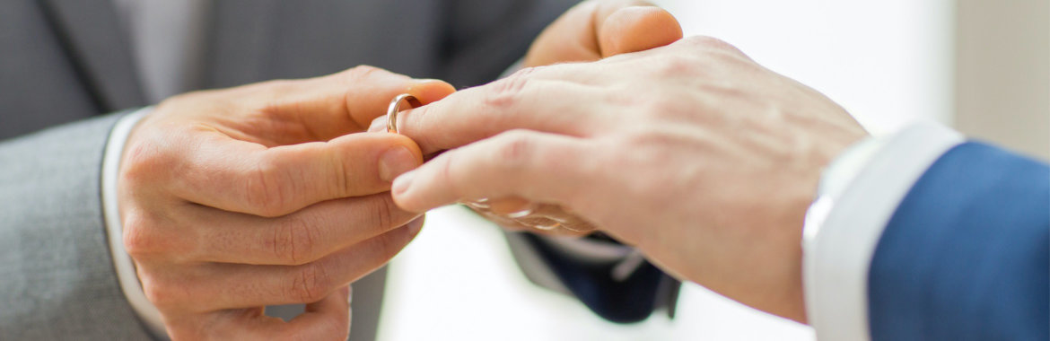 Closeup of man's hands as he puts a wedding ring on his husband's finger.