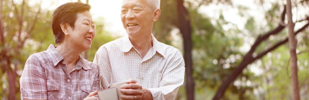 Elderly Asian couple smiling together outdoors.