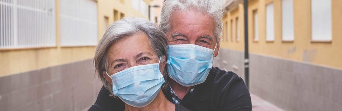 Senior couple embraces while wearing facemasks.