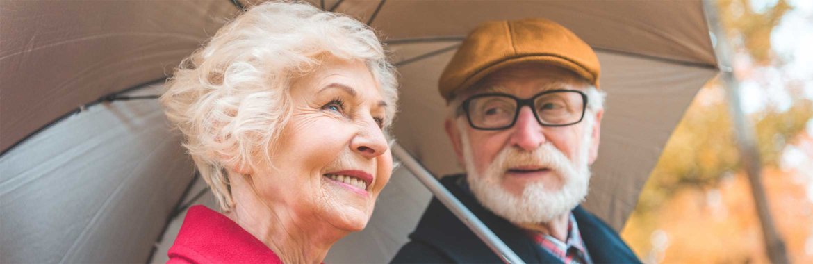 Elderly couple walking in the rain under an umbrella.