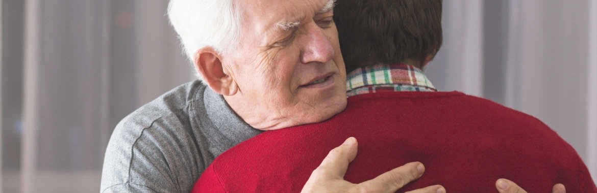 Elderly man embraces caregiving relative.
