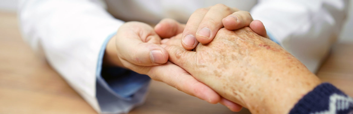 A doctor holds the hand of an older Medicare patient.