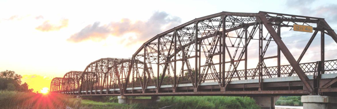 An old metal bridge cuts through the Oklahoma countryside as the sun sets.