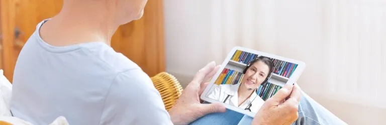Person using a tablet for a video call with a medical professional wearing a headset.