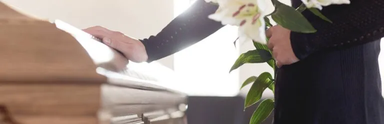 A person in black places a hand on a wooden coffin and holds white lilies during a funeral service.