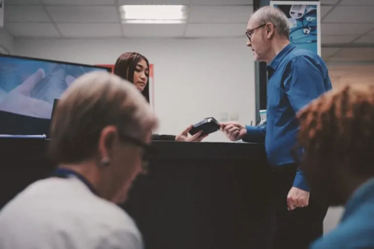 A senior man paying with a card to a receptionist in a hospital lobby