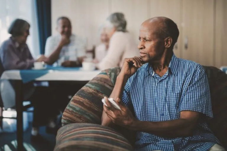 A senior man sitting in a chair, with his senior friends seated around a table in the background