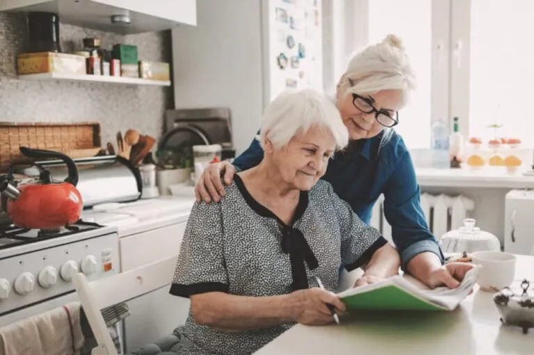 Two women looking at paperwork in a kitchen.