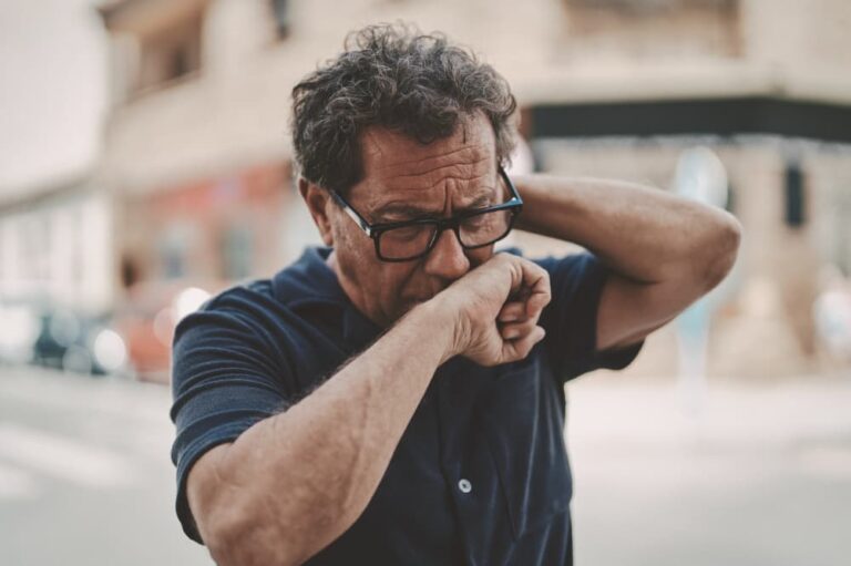 Man outside, coughing into the back of his hand.