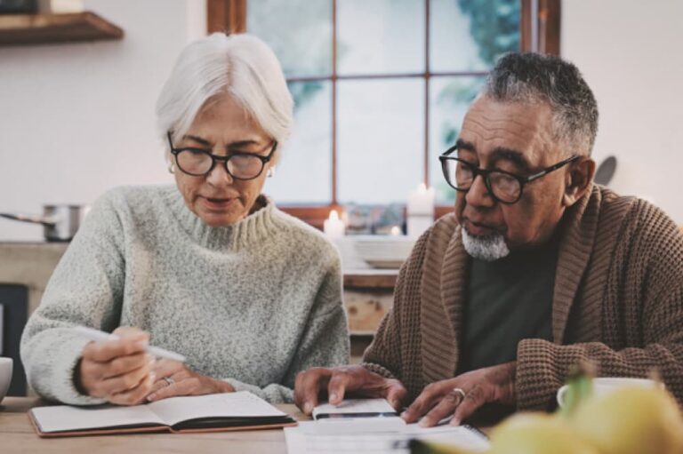 Spectacled senior woman and man sitting at table looking over documents together