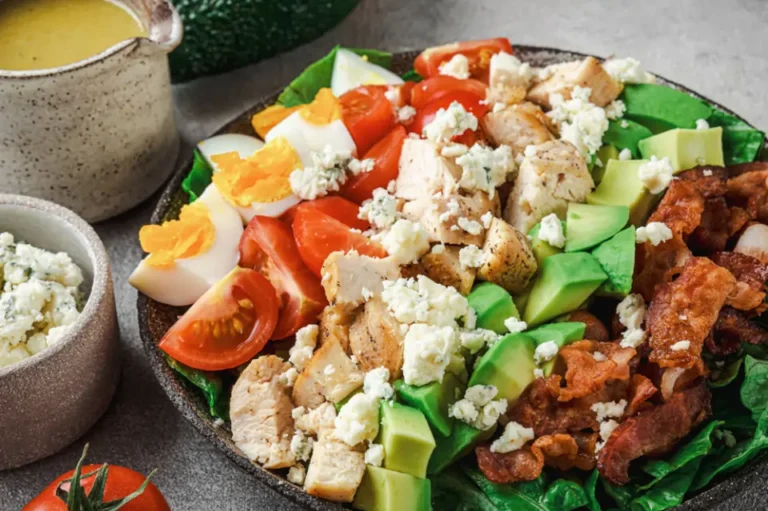 A bowl of Cobb salad featuring crumbled cheese, egg, chicken, avocado, and bacon.