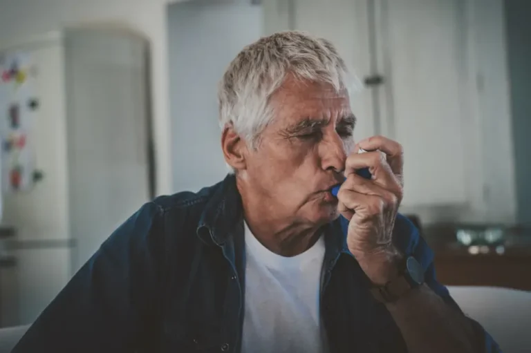 An older man using an inhaler to manage asthma symptoms.